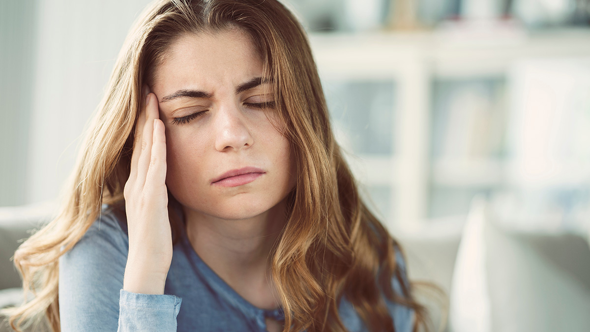 Young woman holding her head in discomfort, experiencing a headache or migraine.