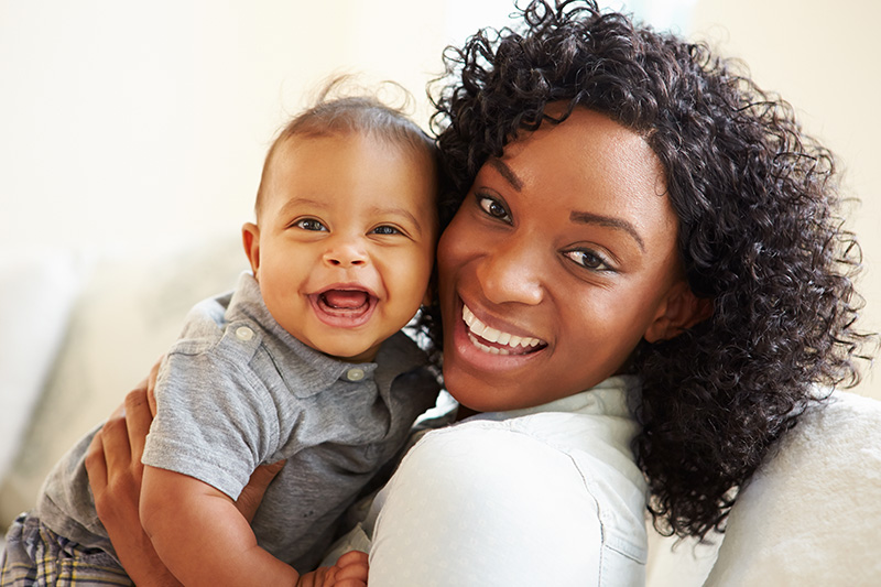 Smiling mother holding her happy baby boy, showcasing joyful parenting moments.