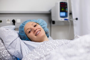 Young patient in scrub cap recovering after surgery in post operative care room.